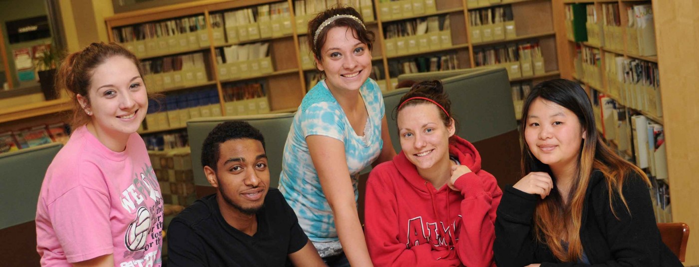 Group of five students in a library smiling