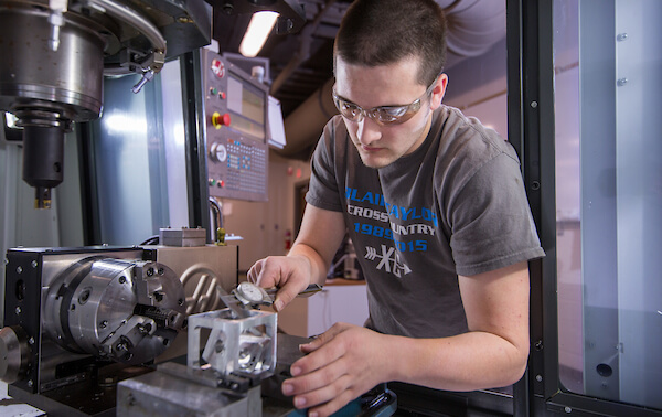 student works on a machine in a machine shop on campus